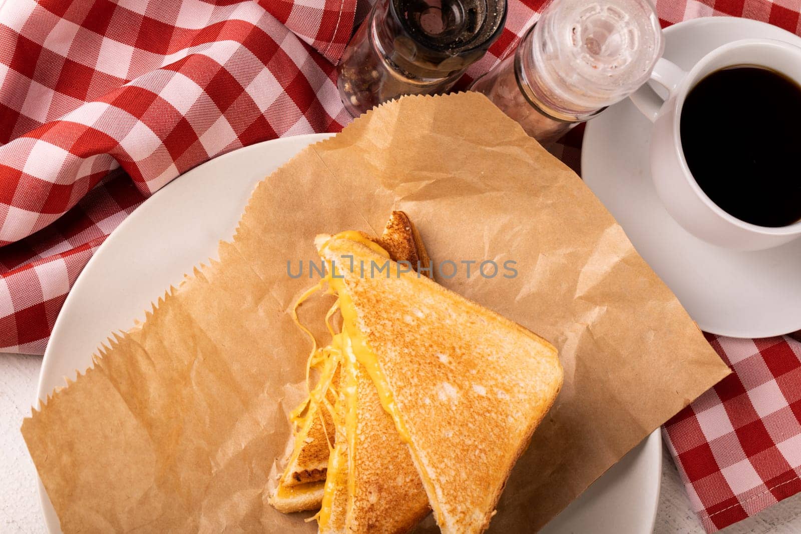 High angle view of fresh cheese sandwich on wax paper in plate by black coffee on table. unaltered, food, unhealthy eating and snack concept.