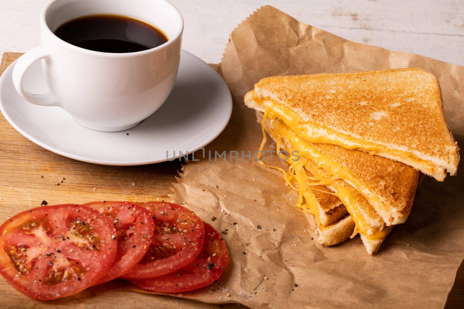 High angle view of fresh black coffee with tomato slices by cheese sandwich on wax paper by Wavebreakmedia