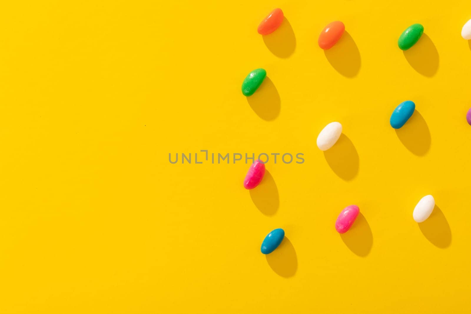 Directly above view of multi colored candies arranged by copy space on yellow background. unaltered, sweet food and unhealthy eating concept.