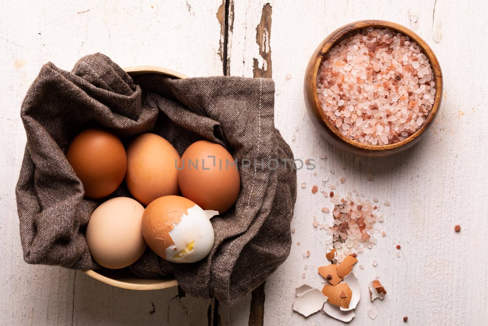 Directly above view of fresh fresh boiled eggs with rock salt in bowls on wooden table by Wavebreakmedia