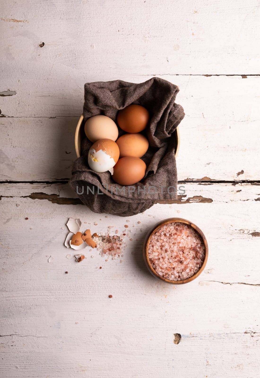 Directly above view of boiled brown eggs and napkin in bowl by rock salt over white wooden table by Wavebreakmedia