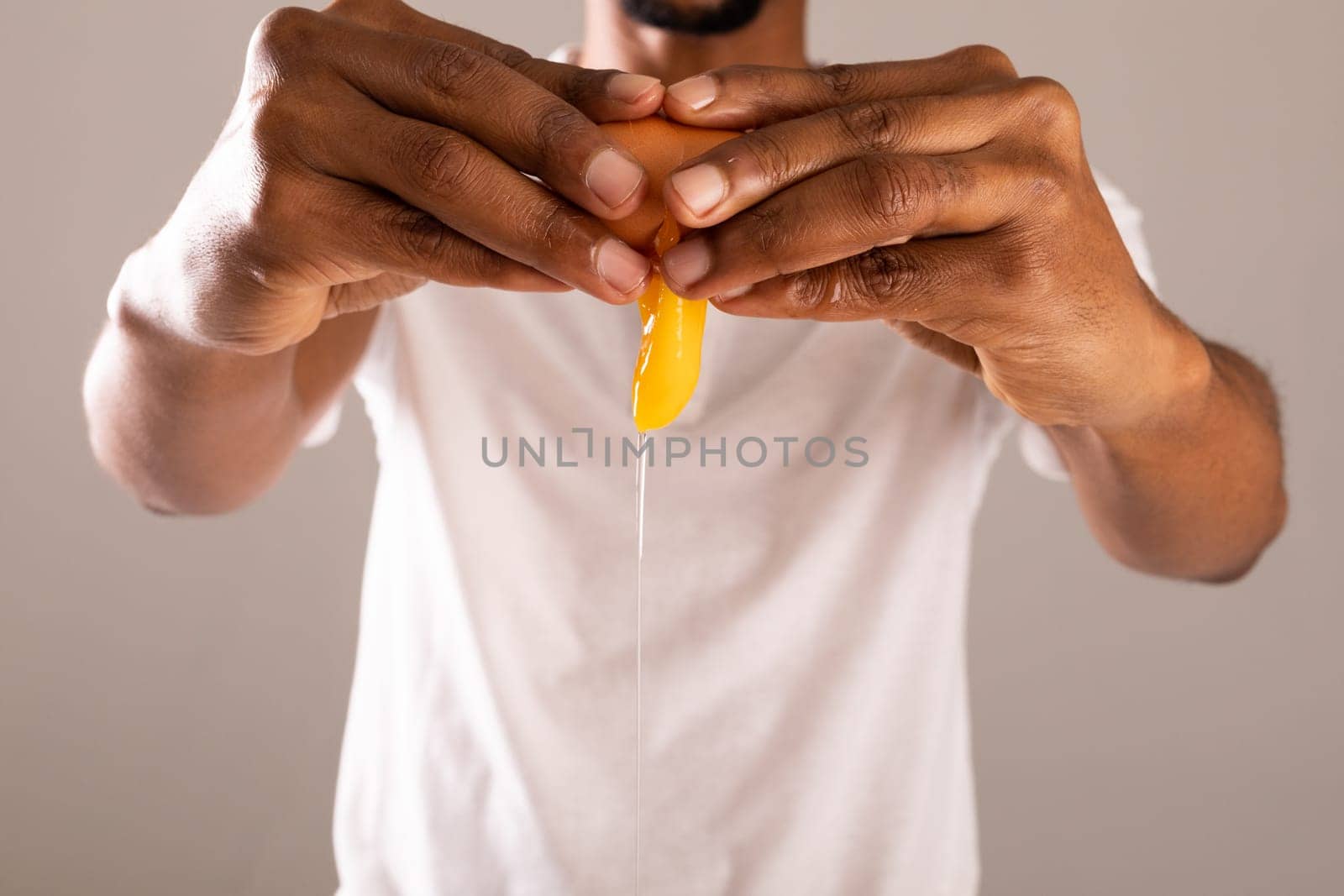 Midsection of man breaking egg shell against gray background by Wavebreakmedia