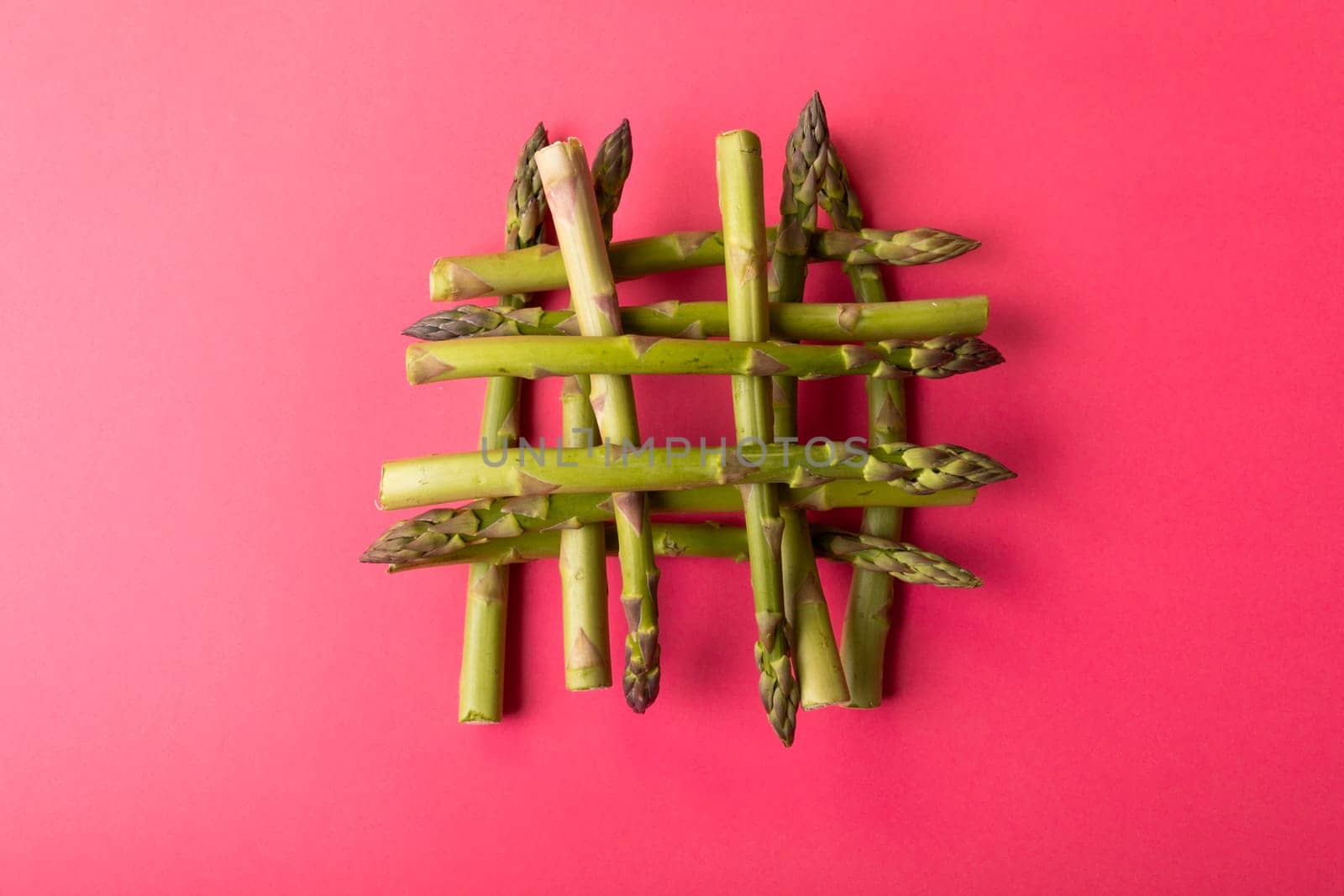 Overhead view of fresh green asparagus stacked on pink background amidst copy space. unaltered, food, healthy eating and organic concept.