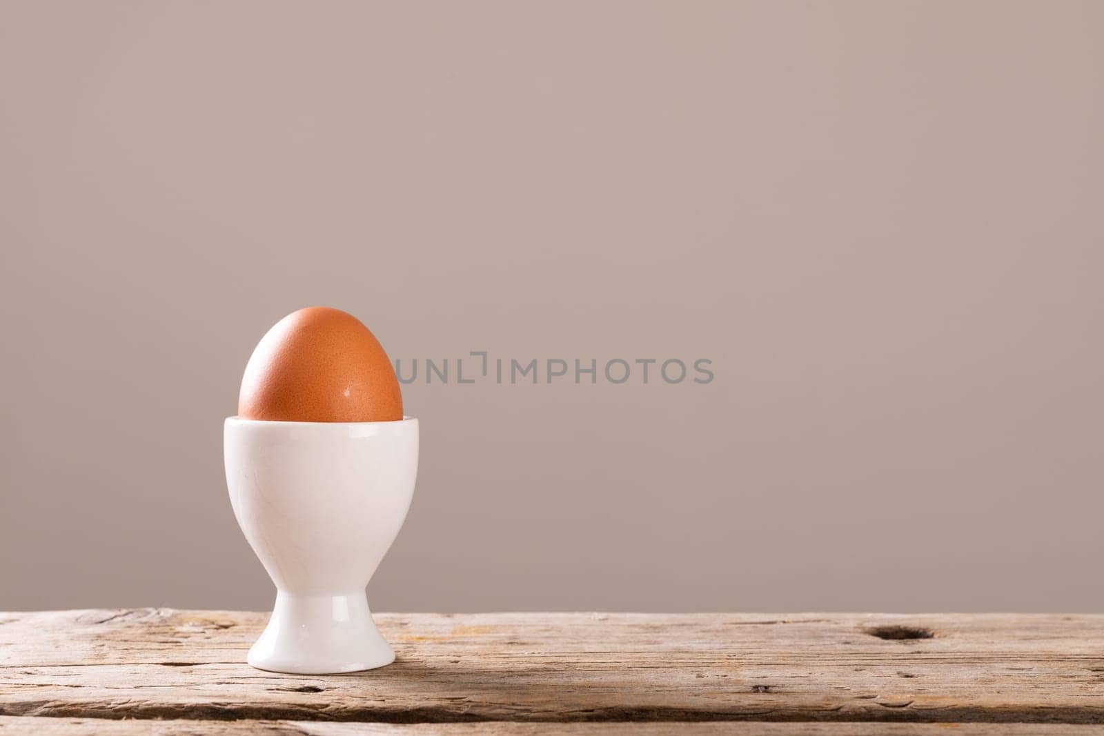 Close-up of boiled brown egg in white cup on wooden table against gray background with copy space by Wavebreakmedia