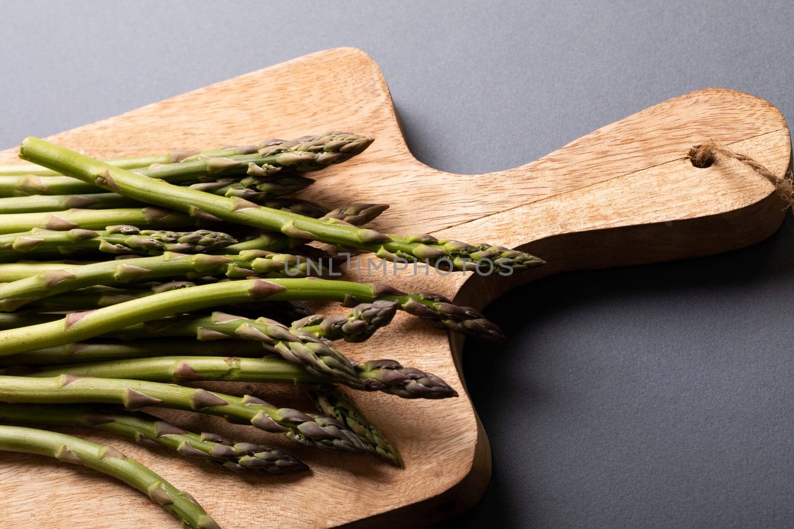 High angle view of fresh green asparagus on wooden cutting board over gray background by Wavebreakmedia