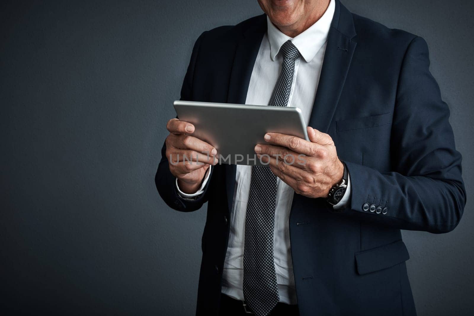 9 to 5 is a thing of the past. Studio shot of a mature businessman using his digital tablet. by YuriArcurs