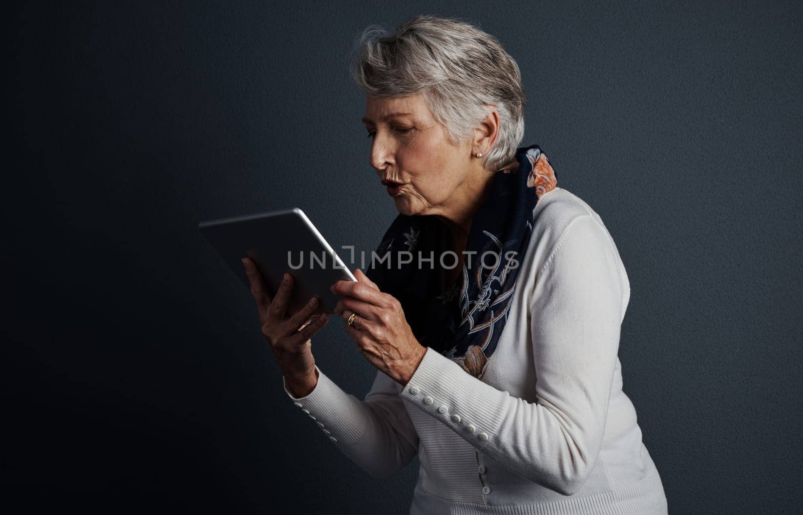 I really would like to own one of these. Studio shot of a cheerful elderly woman standing and giving her tablet a kiss. by YuriArcurs