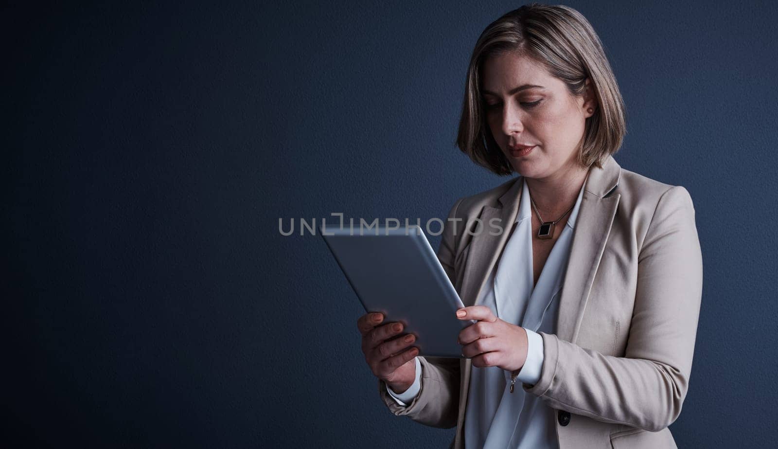 Everything is just a tap away. Studio shot of an attractive young corporate businesswoman using a tablet against a dark background. by YuriArcurs
