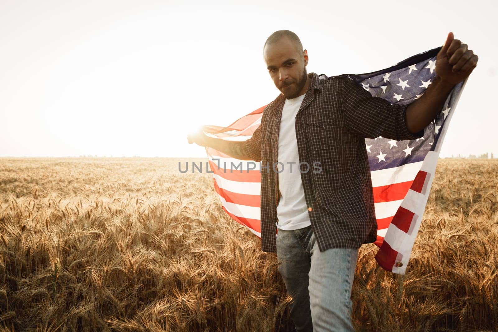 African american young man holding USA national flag through wheat field by Fabrikasimf