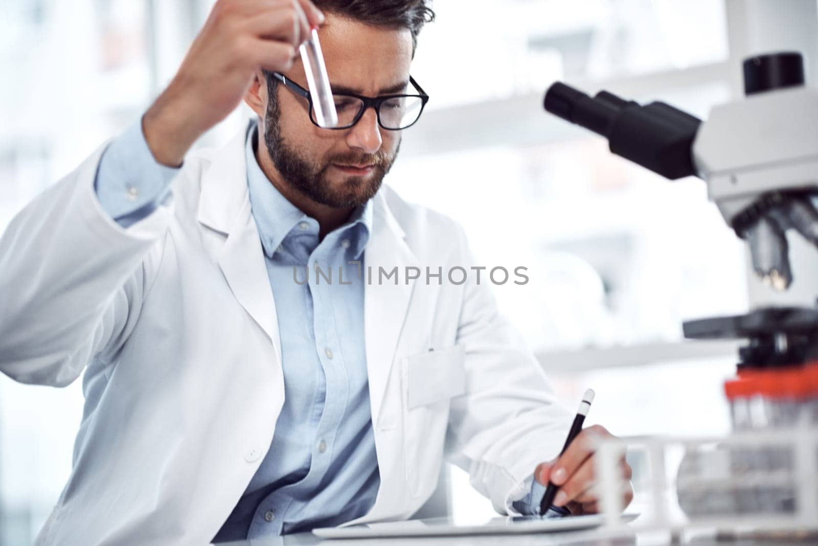 Another one for the records. a focused young male scientist making notes while holding up a test tube inside of a laboratory. by YuriArcurs