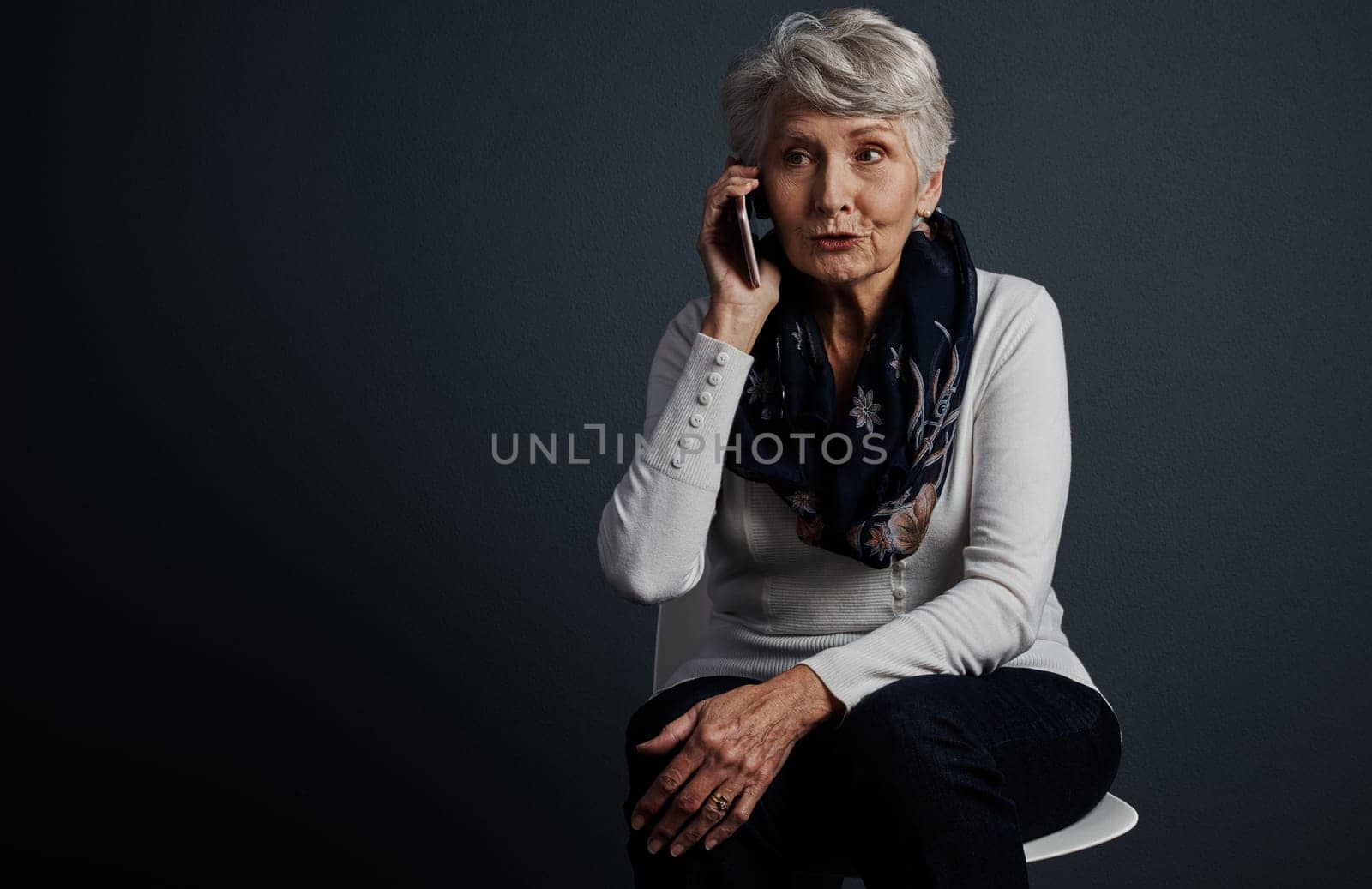 I love this contraption. Studio shot of a cheerful elderly woman sitting down and talking on her cellphone. by YuriArcurs