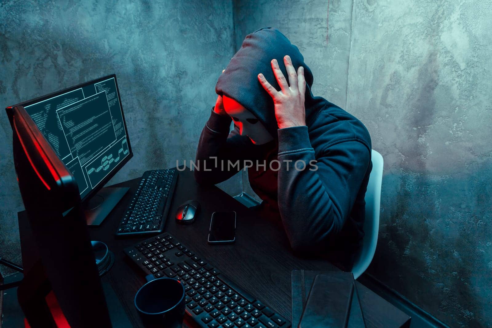 Anonymous internet hacker with mask sitting at the table and using computer in the dark
