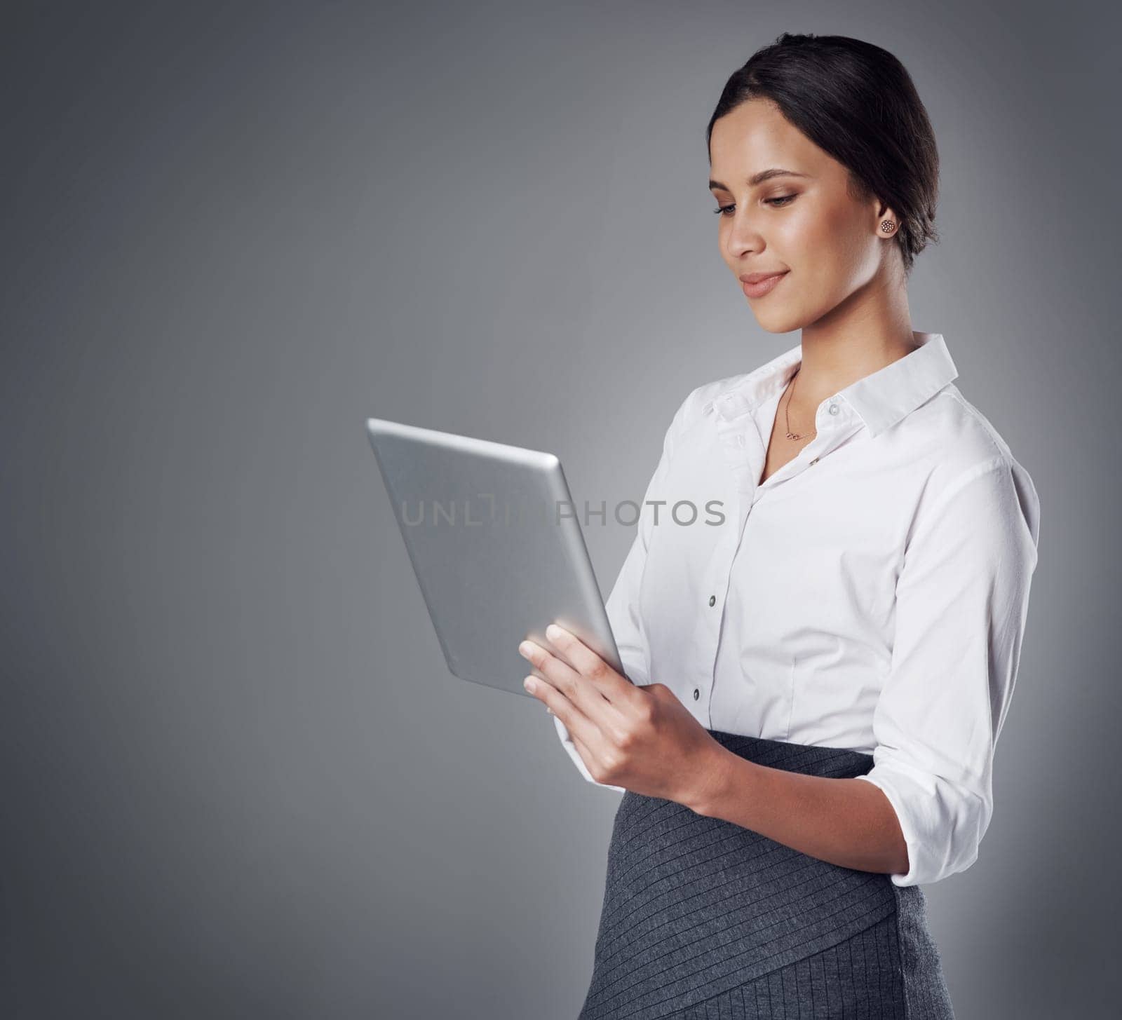 Keeping up with competitive business using cutting edge technology. Studio shot of a young businesswoman using a digital tablet against a gray background. by YuriArcurs