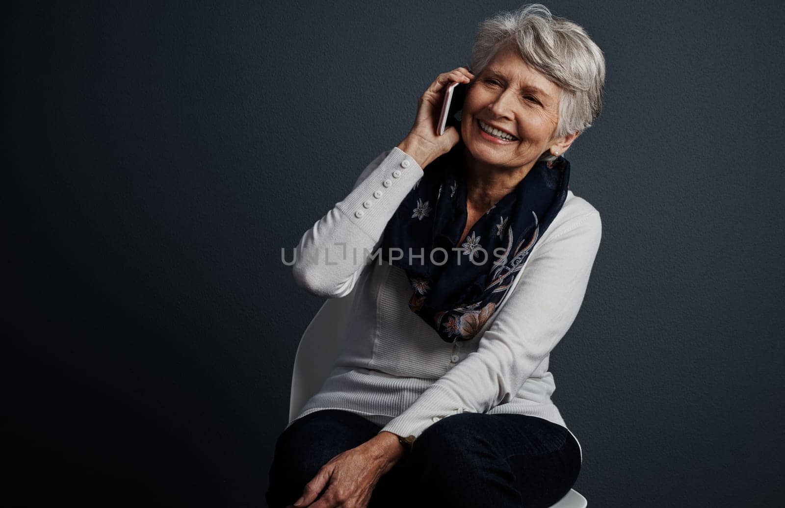 Yes I do indeed own a cellphone. Studio shot of a cheerful elderly woman sitting down and talking on her cellphone