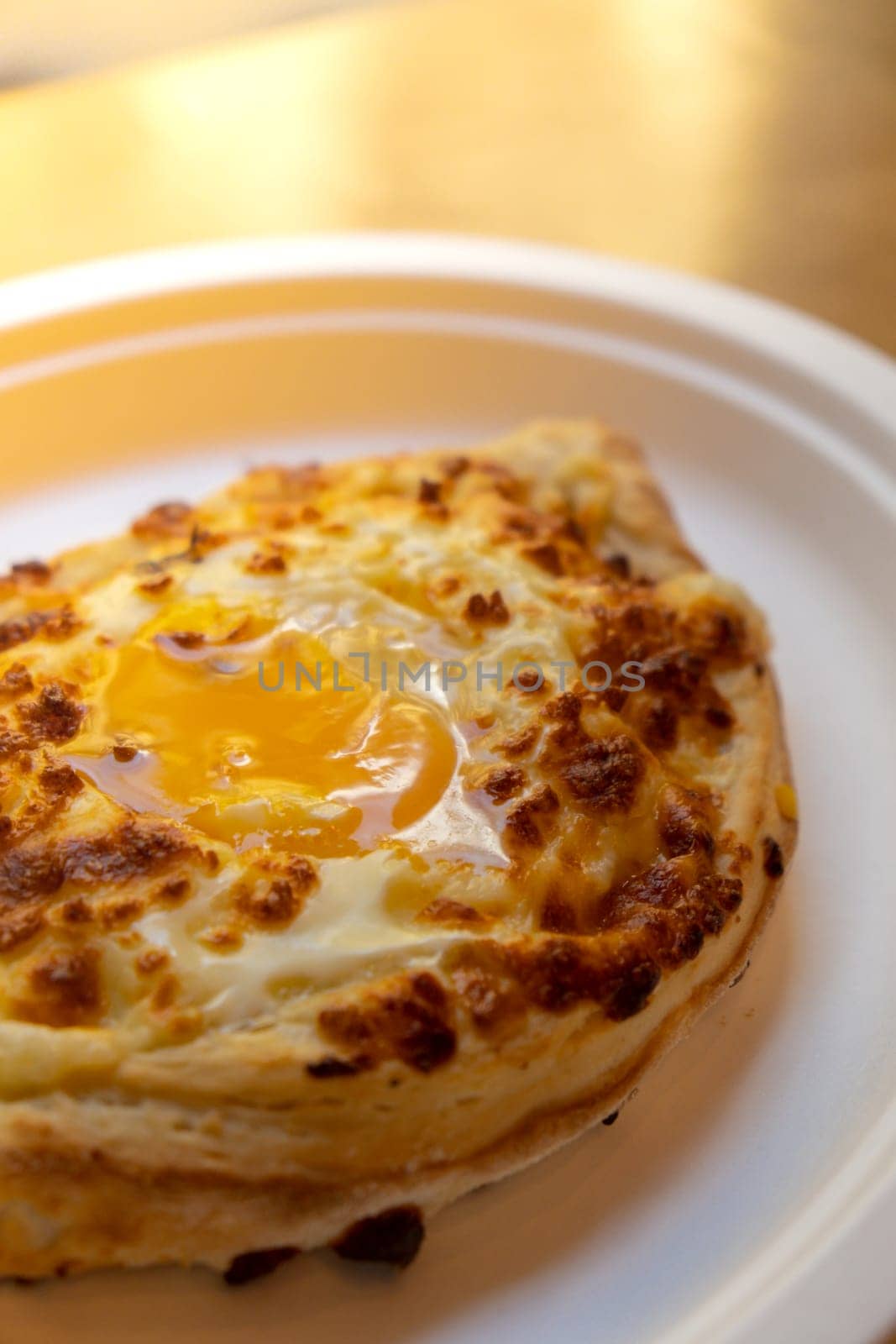 Traditional Georgian cuisine. Ajara khachapuri on paper plate. Filled with cheese and topped with raw egg and butter, cheese-filled bread. Delicious food