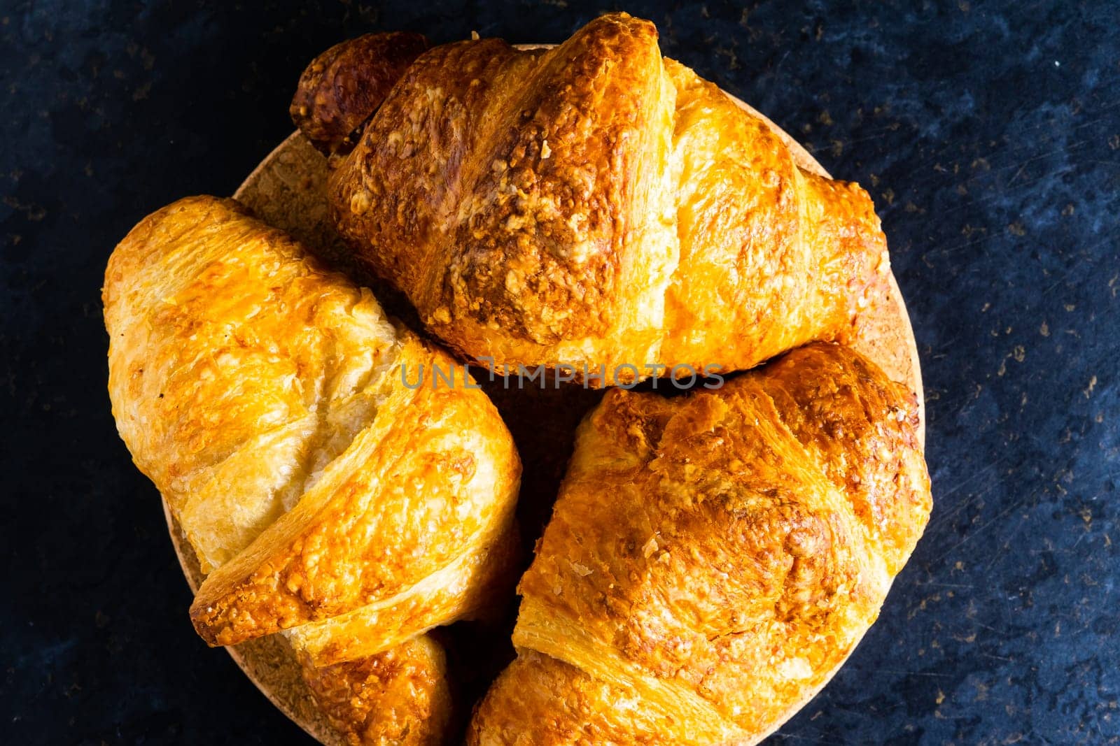 Freshly backed french croissant shiny in the rays of morning sun, dark background, kitchen