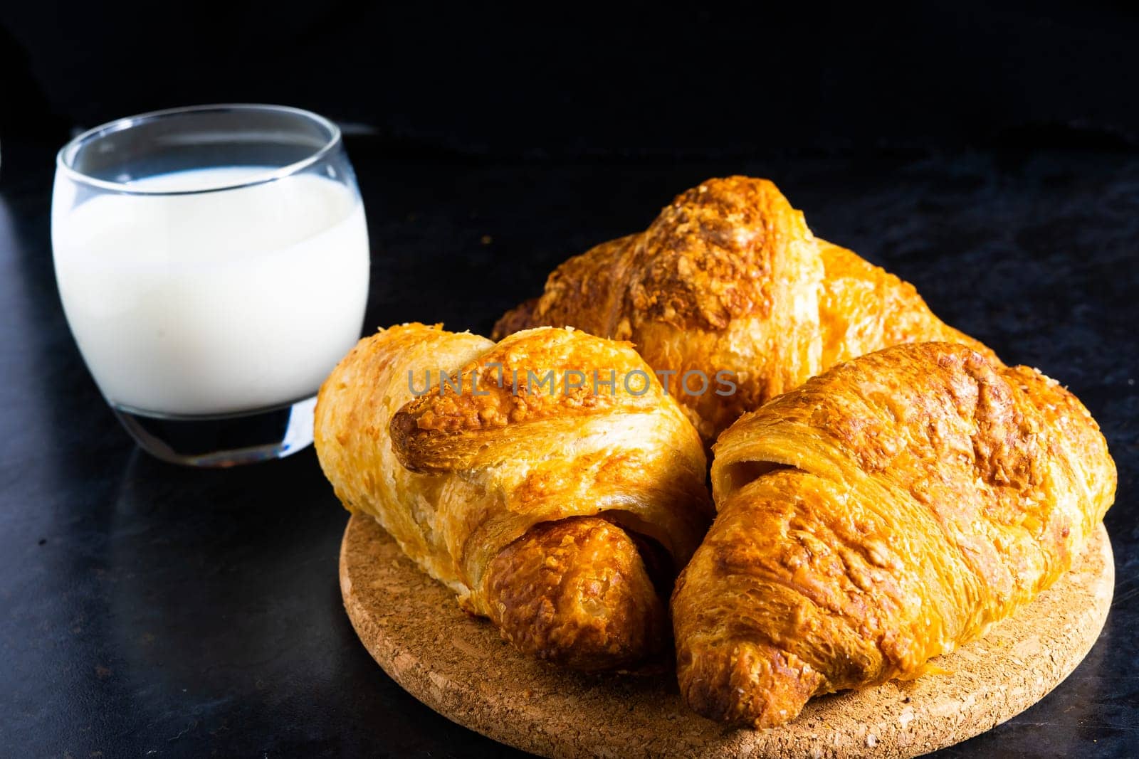 Freshly backed french croissant shiny in the rays of morning sun, dark background, kitchen