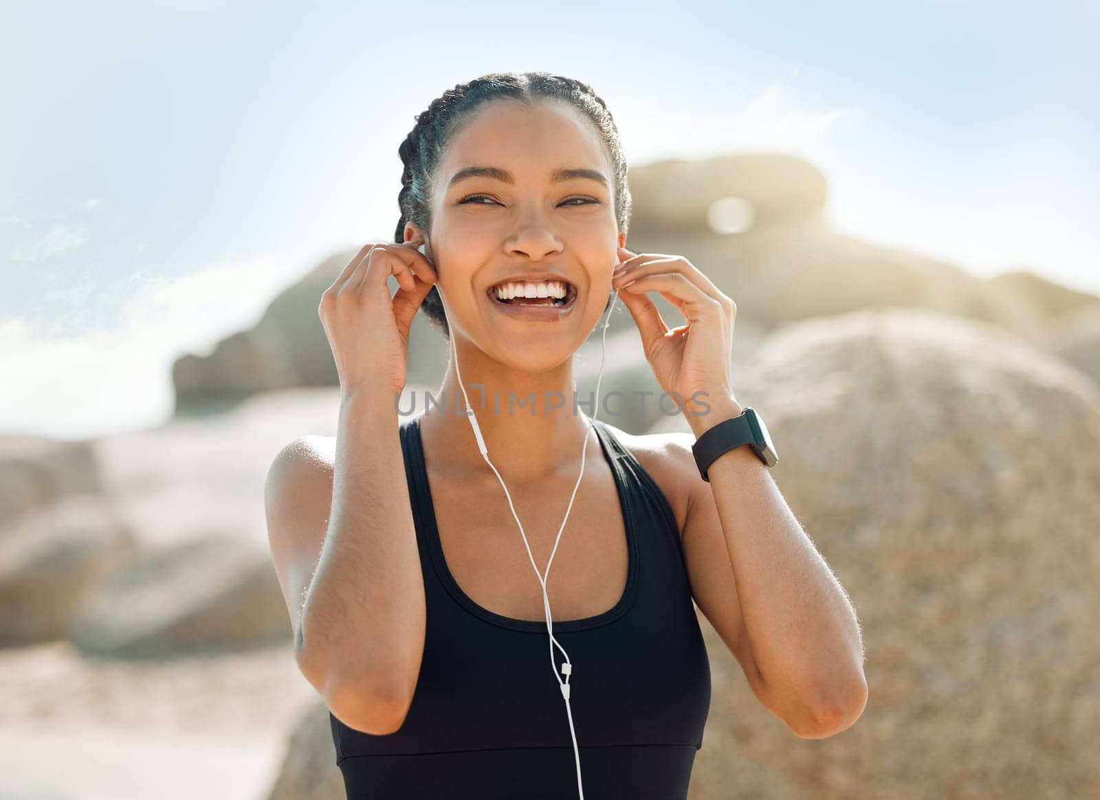 Happy woman with earphones, fitness at the beach and listening to music for motivation and workout outdoor. Exercise, health and smile, female athlete streaming online with radio and audio in nature.
