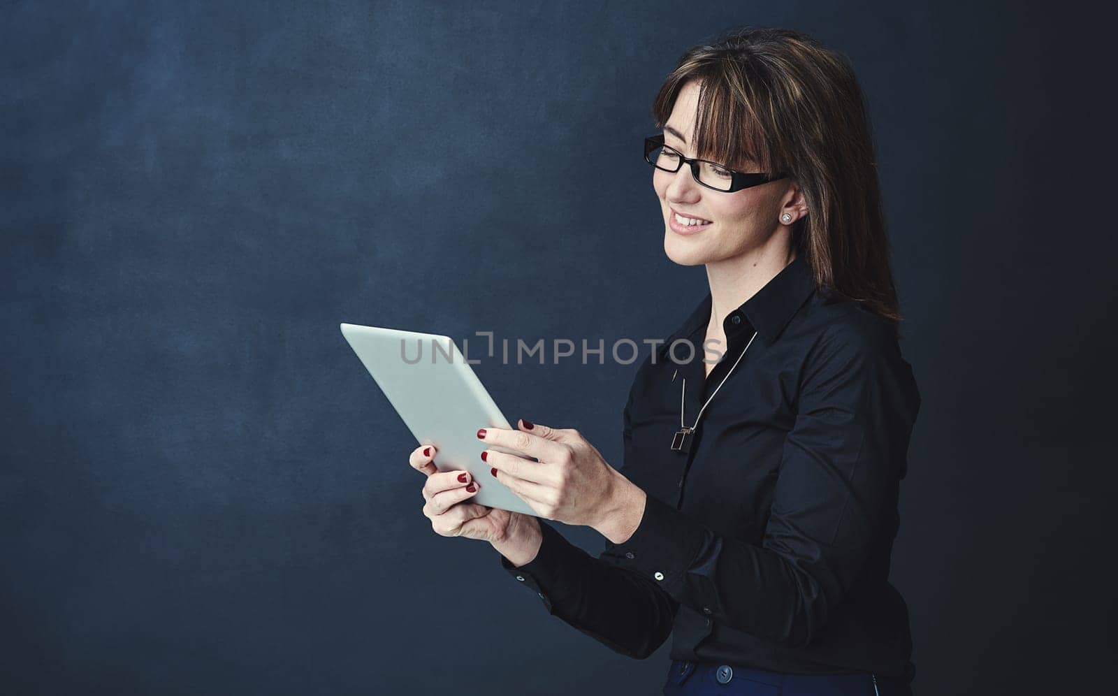 Organising her plans for success the smart way. Studio portrait of a corporate businesswoman using a digital tablet against a dark background. by YuriArcurs