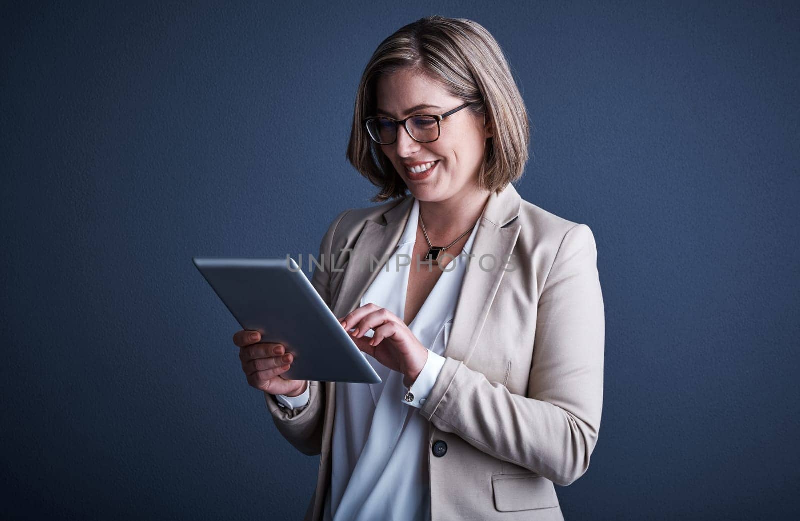 This is wonderful. Studio shot of an attractive young corporate businesswoman using a tablet against a dark background