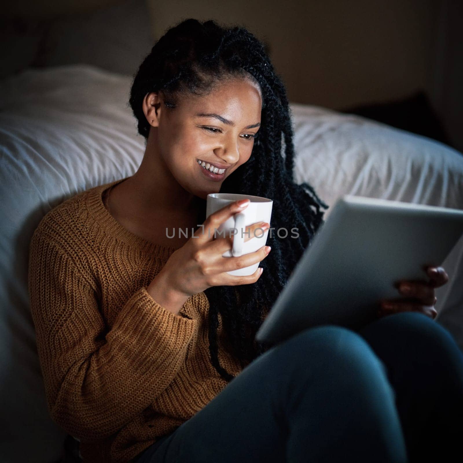 Indulging in some laziness after a long day. a relaxed young woman drinking coffee and using a digital tablet during the evening at home. by YuriArcurs