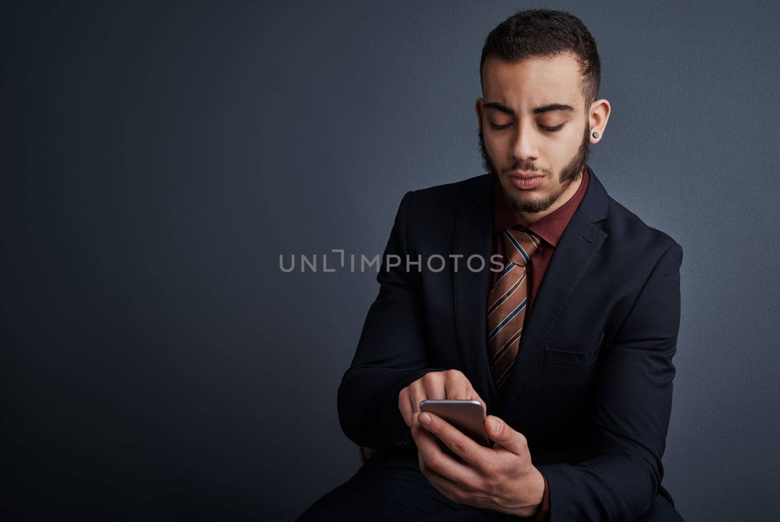 Its communication made simple. Studio shot of a stylish young businessman sending a text message while sitting against a gray background. by YuriArcurs
