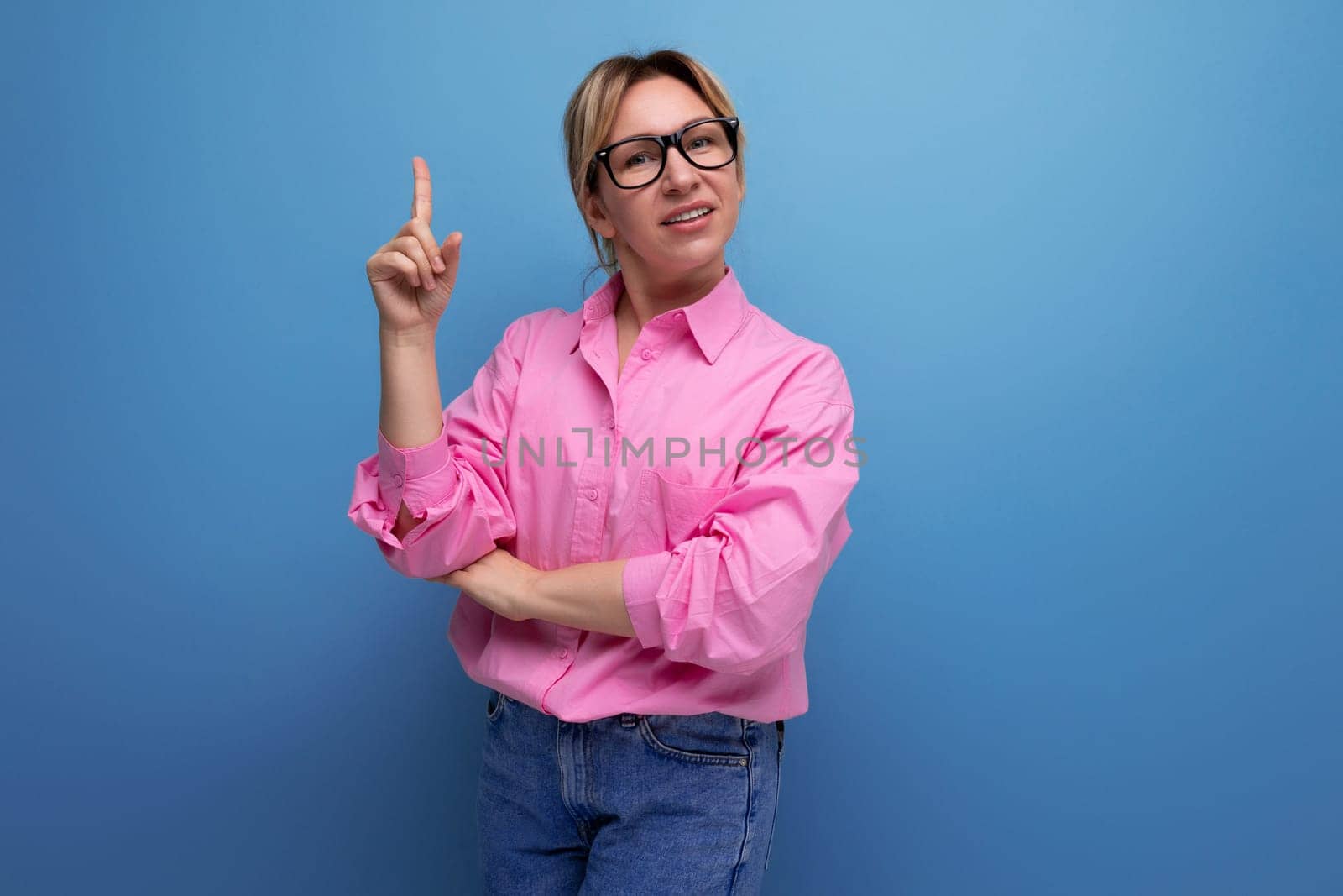 positive european confident young blond businesswoman in pink shirt and jeans on studio background with copy space.