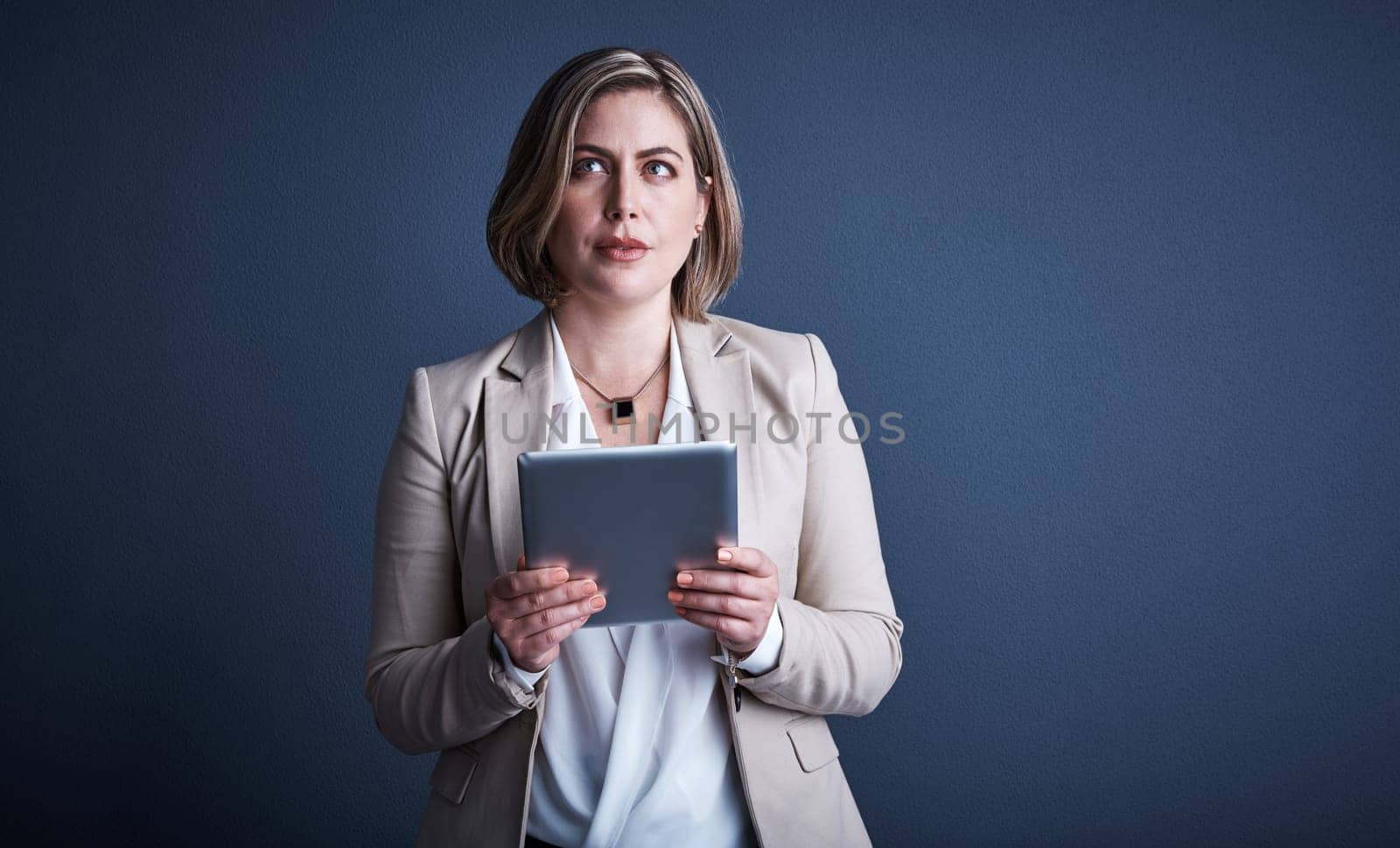 Let me see now...Studio shot of an attractive young corporate businesswoman using a tablet against a dark background