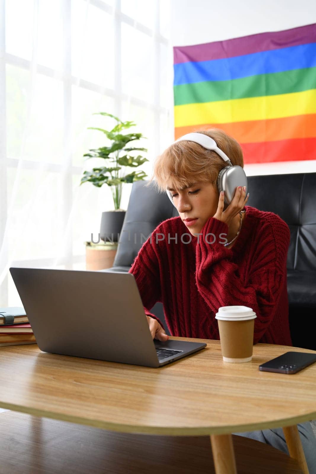 Focused young Asian gay man student in headphone looking at laptop screen watching tutorial, lecture or studying online at home.