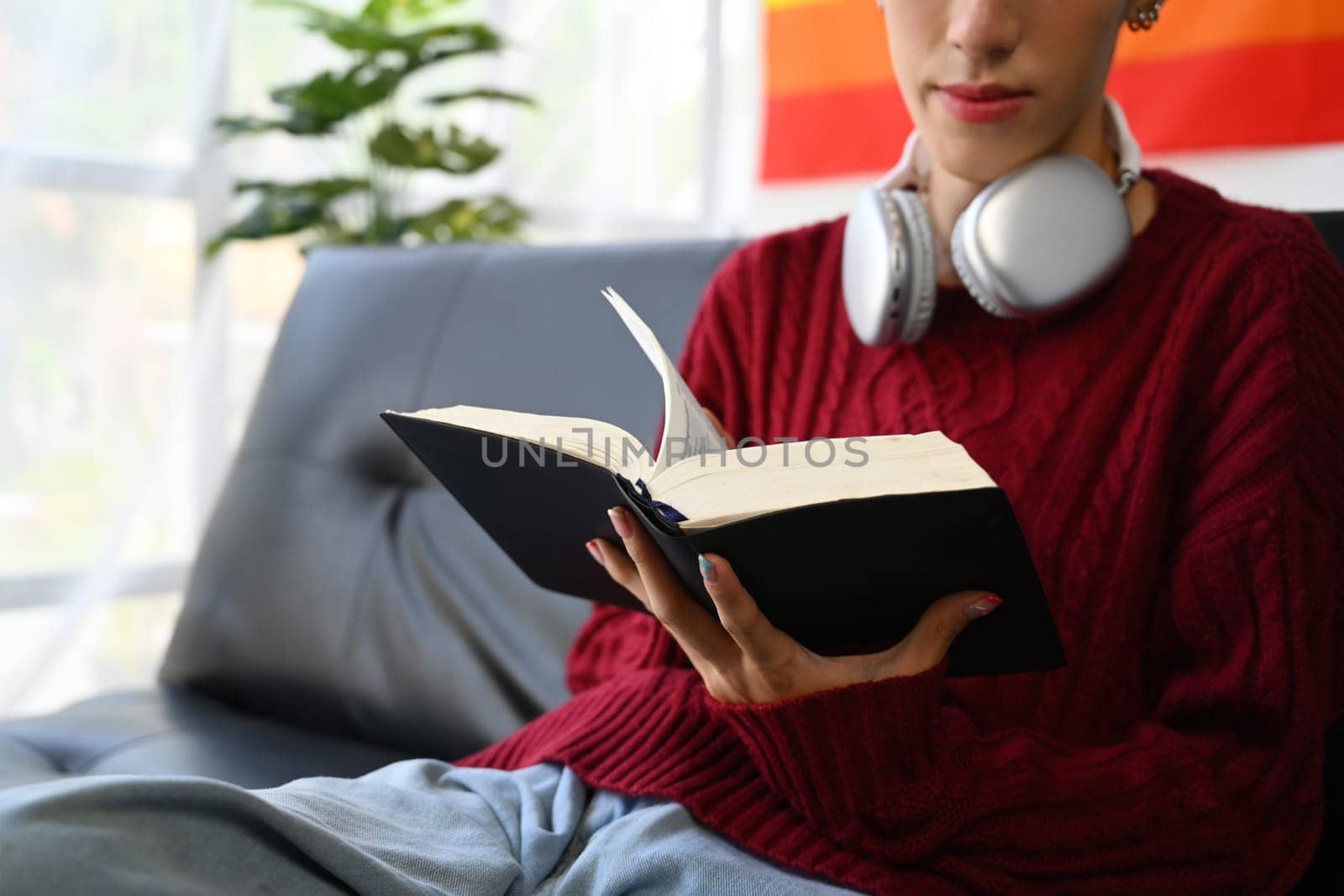 Relaxed young gay man relaxing on couch at home and reading book. LGBTQ, people lifestyle, leisure concept.