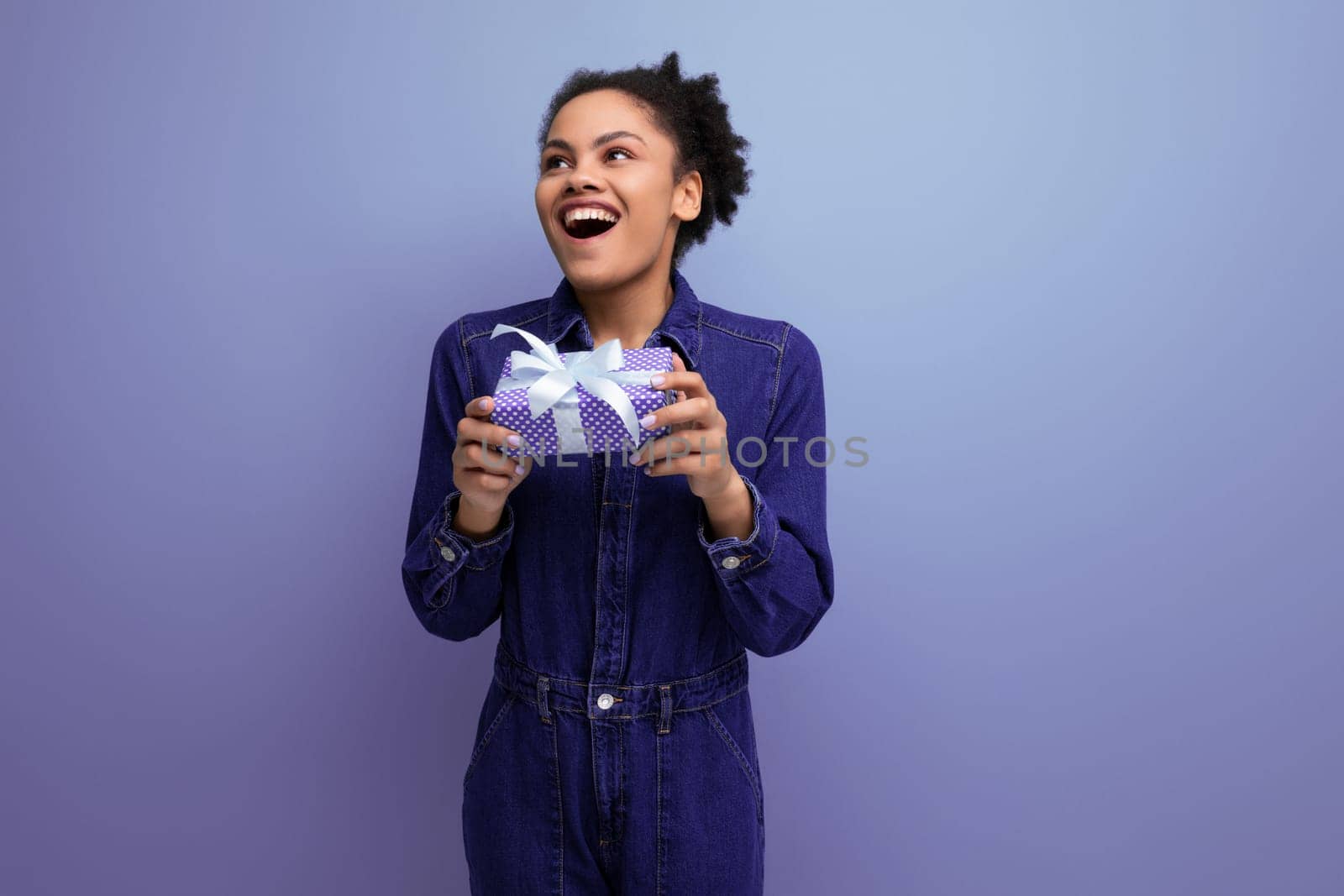 young pretty brunette latin woman with afro ponytail dressed in denim clothes received a gift box by TRMK