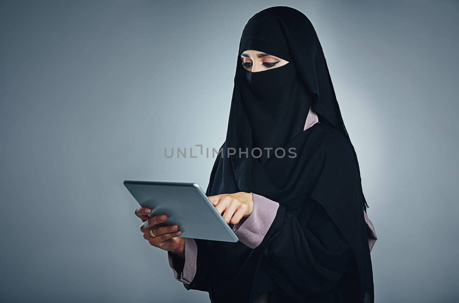 Doing so much with just one touch. Studio shot of a young woman wearing a burqa and using a digital tablet against a gray background