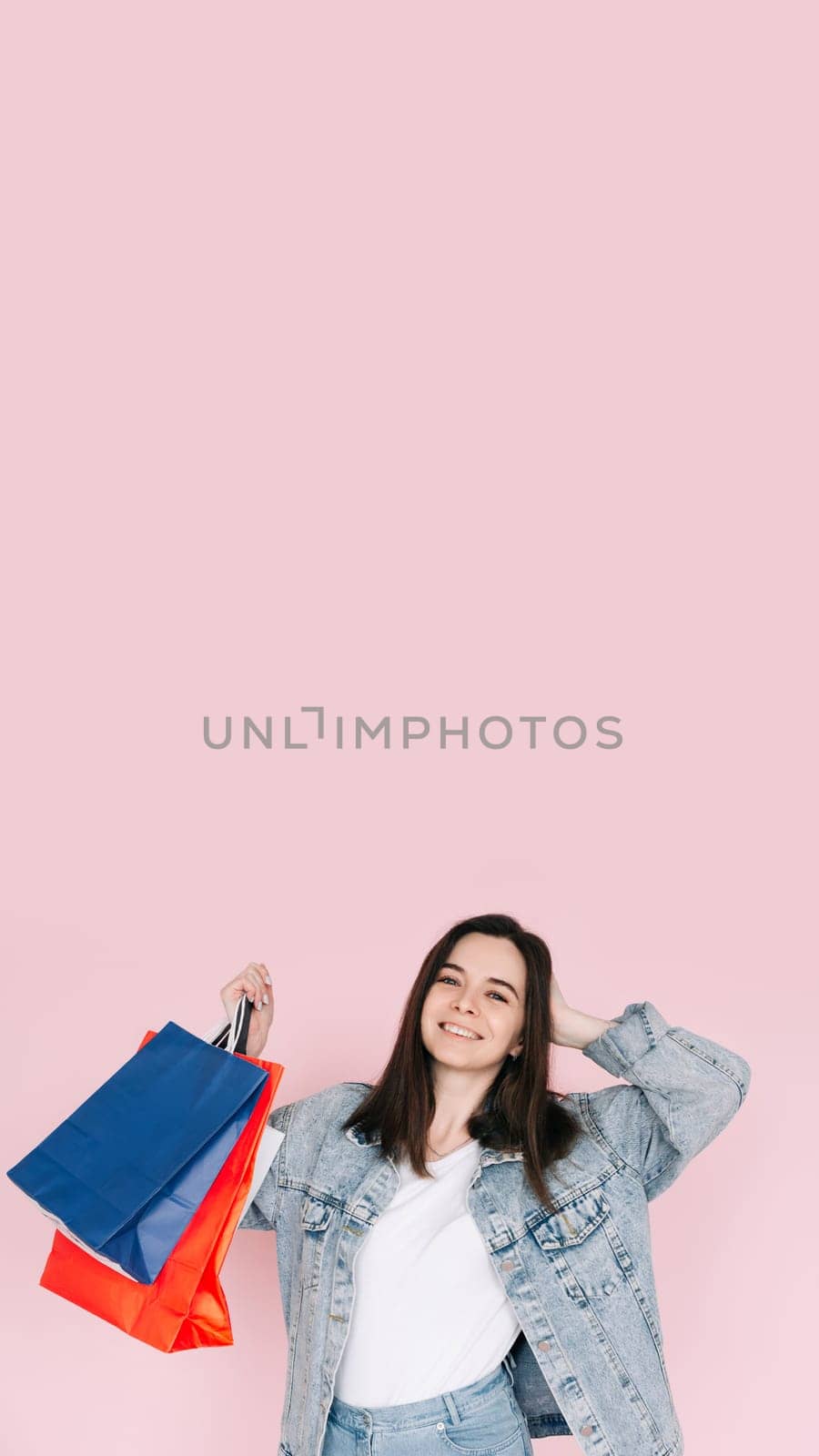 Joyful Shopper: Young Woman in Denim Shirt Celebrating, Arm Raised in Excitement, Against Pink Background, Delighted by Online Shopping or Amazing Find. Vertical photography