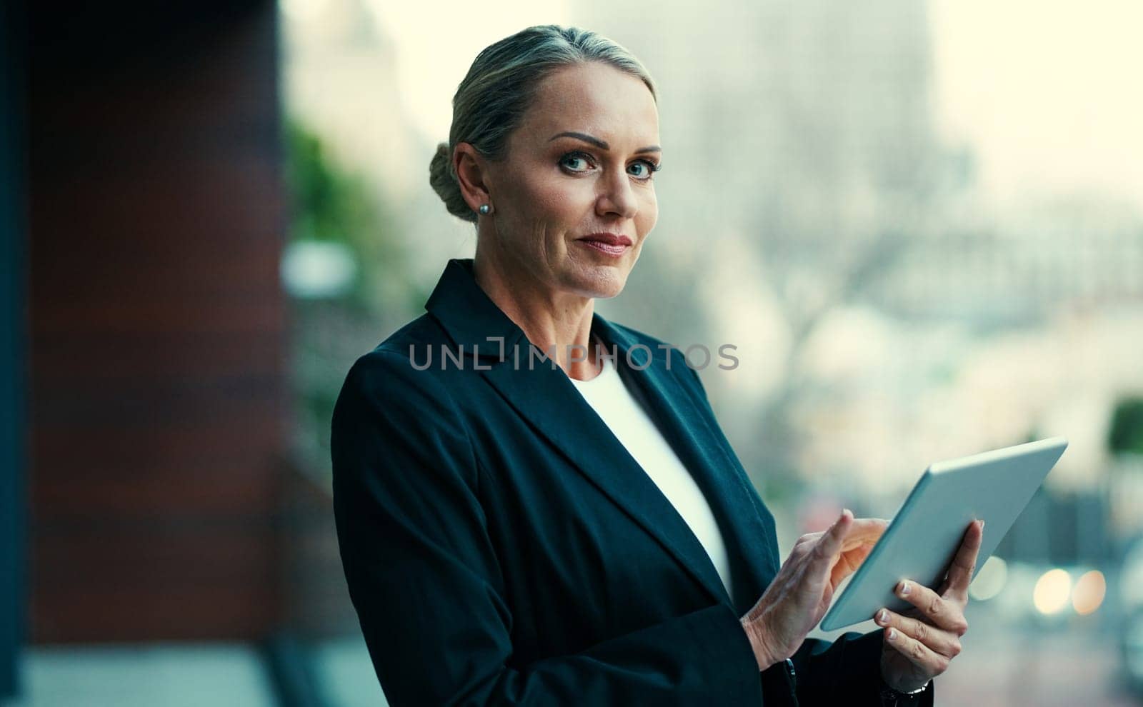 It keeps me current and connected. Portrait of a mature businesswoman standing outside on the balcony of an office and using a digital tablet. by YuriArcurs