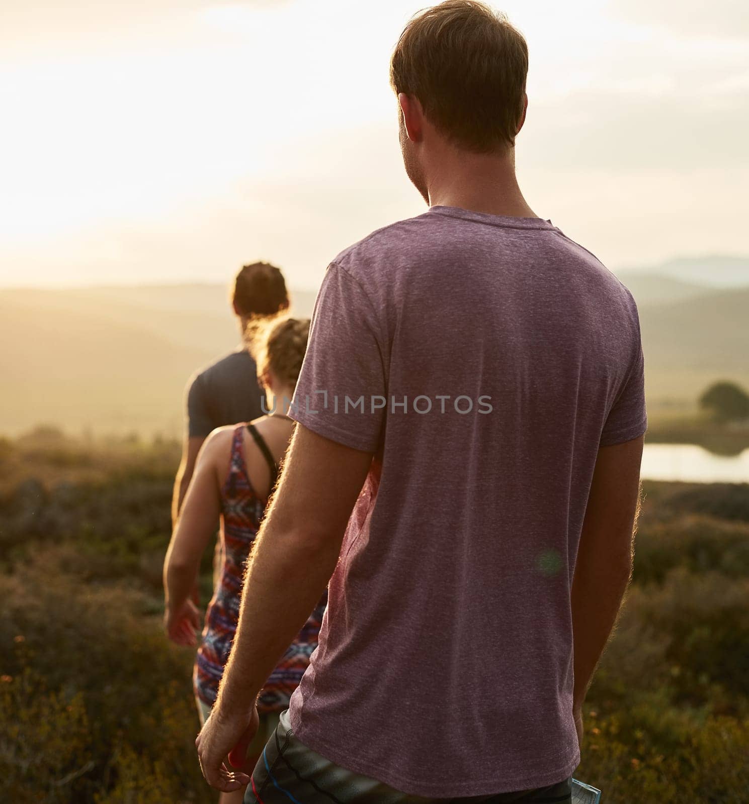 Friends, people hiking and trekking in countryside with fitness at sunset, nature with travel together and freedom. Exercise, adventure with men and woman walk through meadow or field with back view.