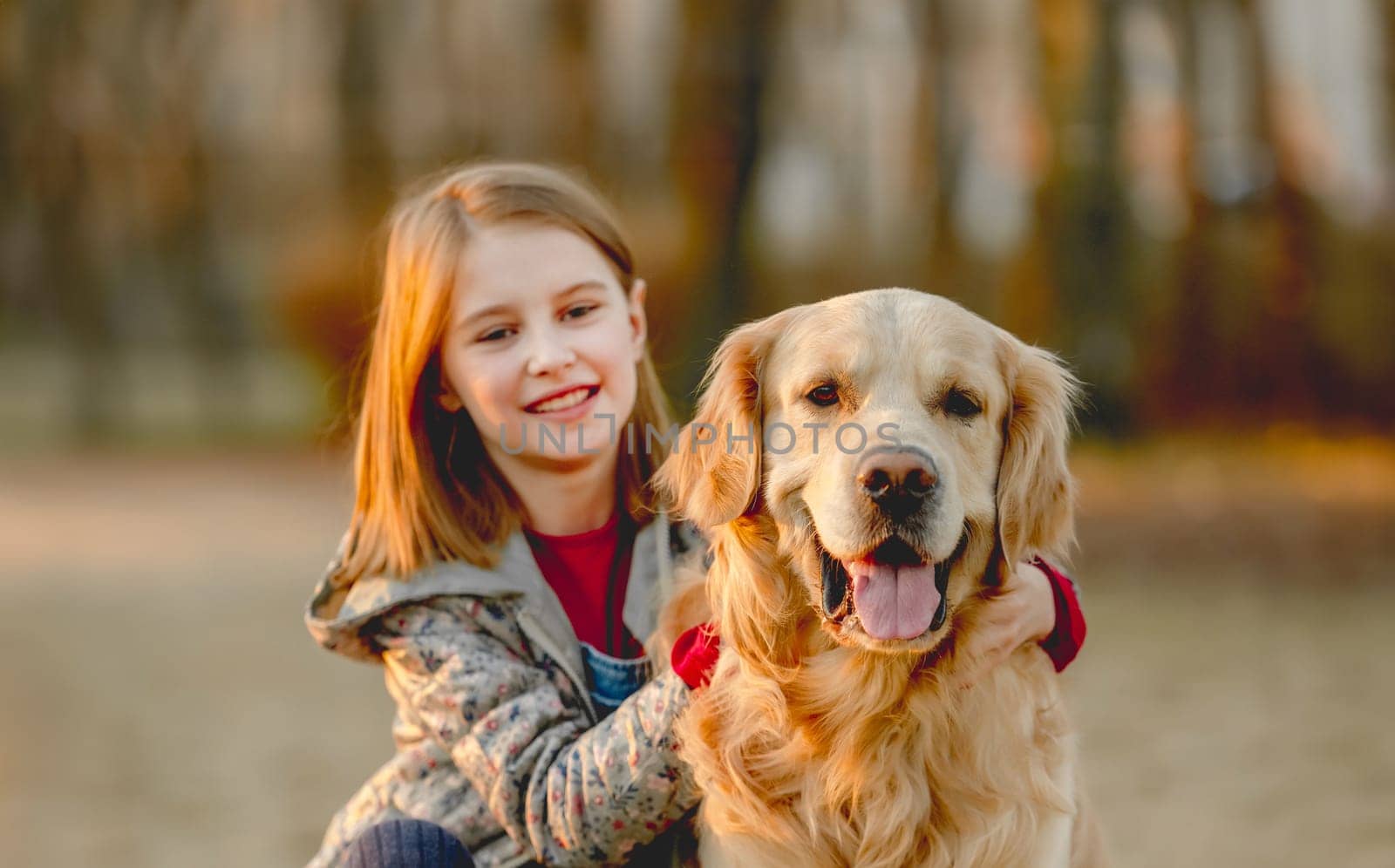 Preteen girl with golden retriever dog sitting in park in beautiful spring autumn day.