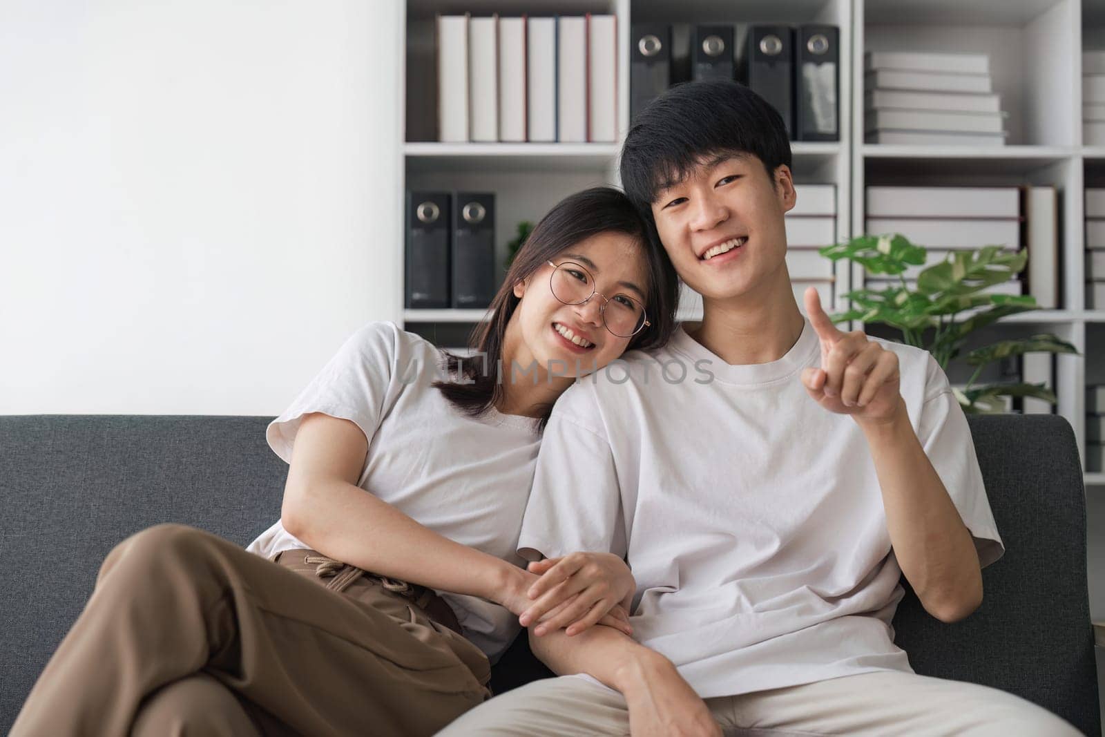 leisure activities. Positive young Asian couple relaxing on sofa, watching TV, enjoying movie together at home.
