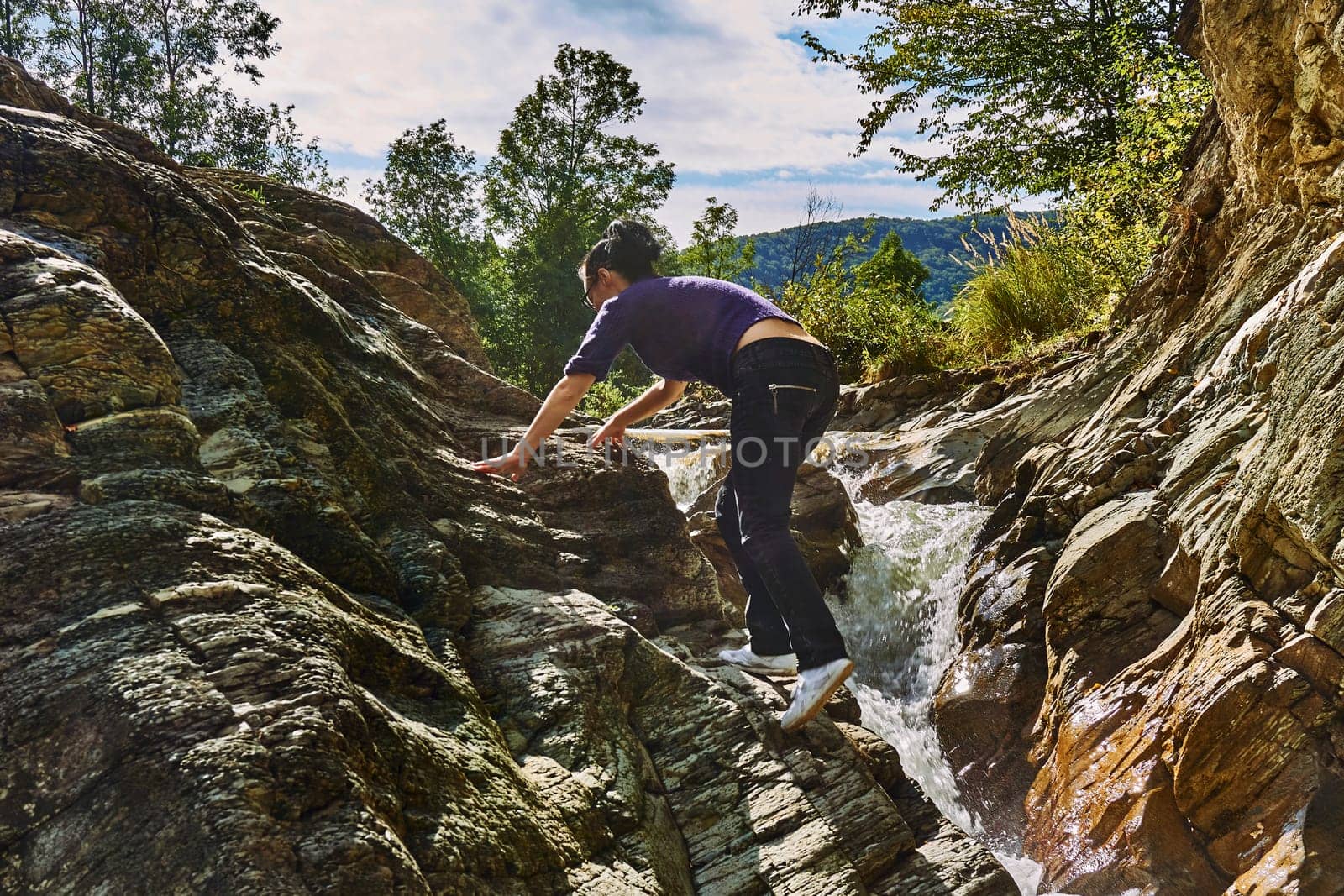 A young female tourist climbs the rocks stones near a mountain stormy river. by jovani68