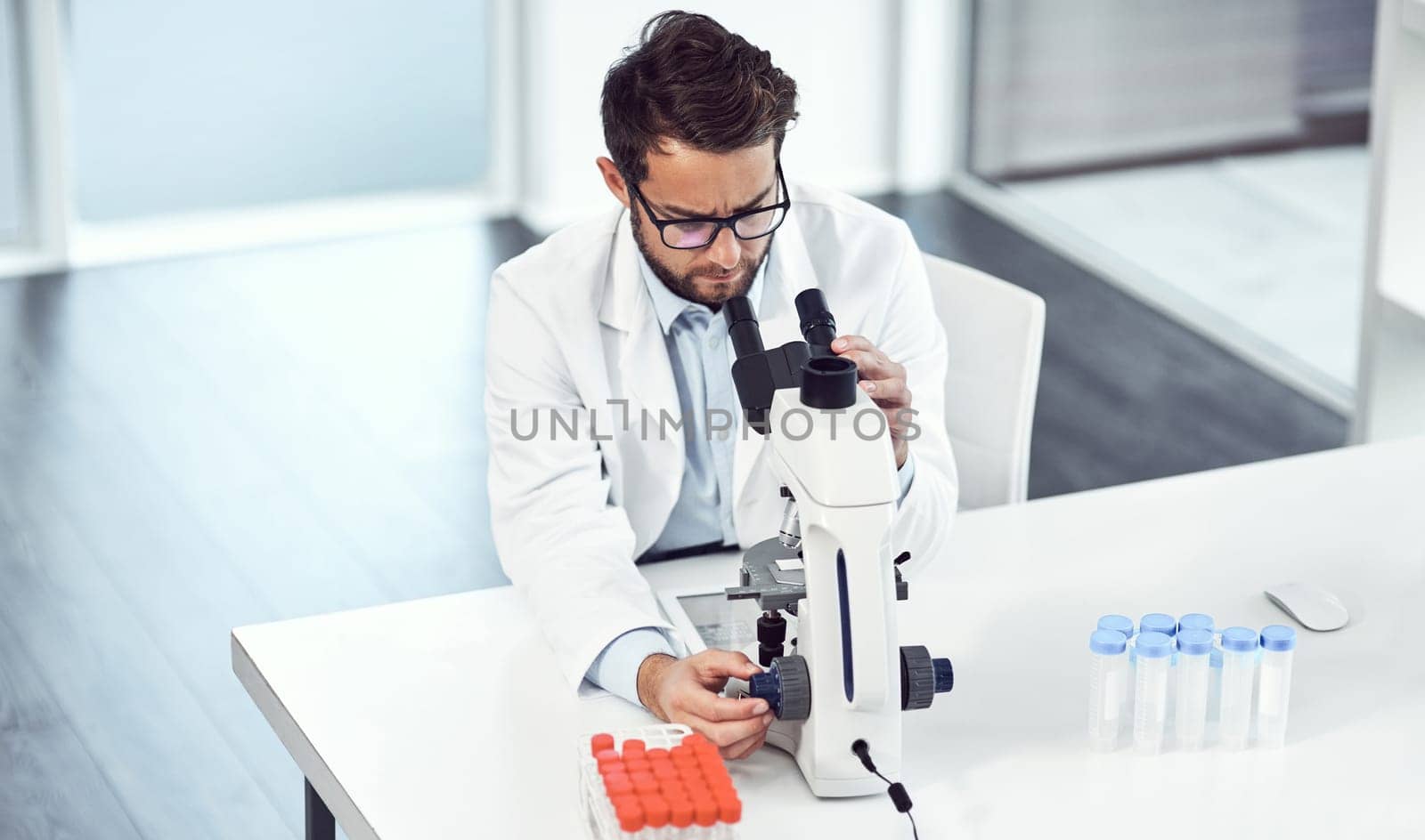 That looks pretty peculiar. a focused young male scientist looking through a microscope inside of a laboratory