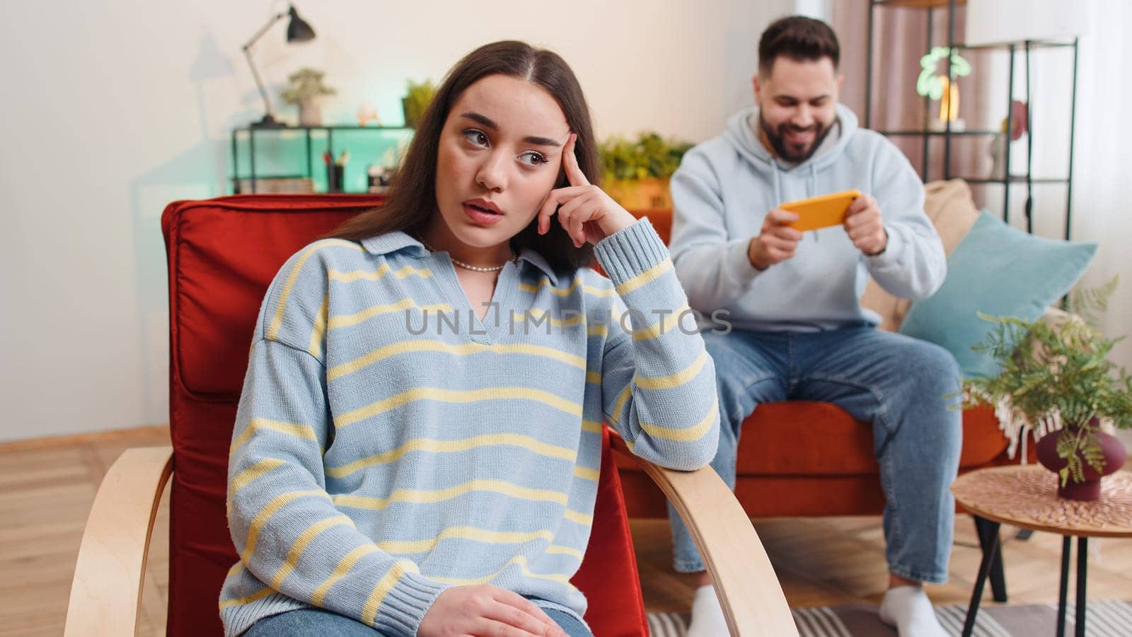Unhappy woman looking at camera, quarreling with man player addicted of game playing on smartphone by efuror
