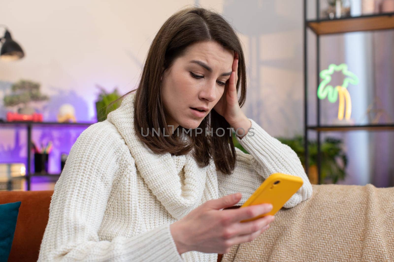 Sad displeased woman use smartphone typing browsing, loses becoming surprised sudden lottery results, bad news, fortune loss, fail, deadline, virus. Portrait of young girl at home living room on couch