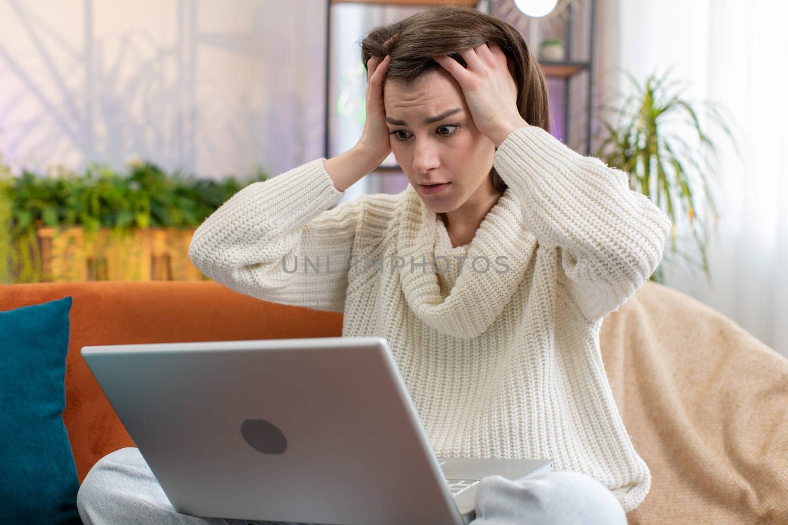 Displeased woman use laptop notebook typing browsing working, loses becoming surprised sudden lottery results bad news fortune loss fail computer virus. Portrait of girl at home in room on couch