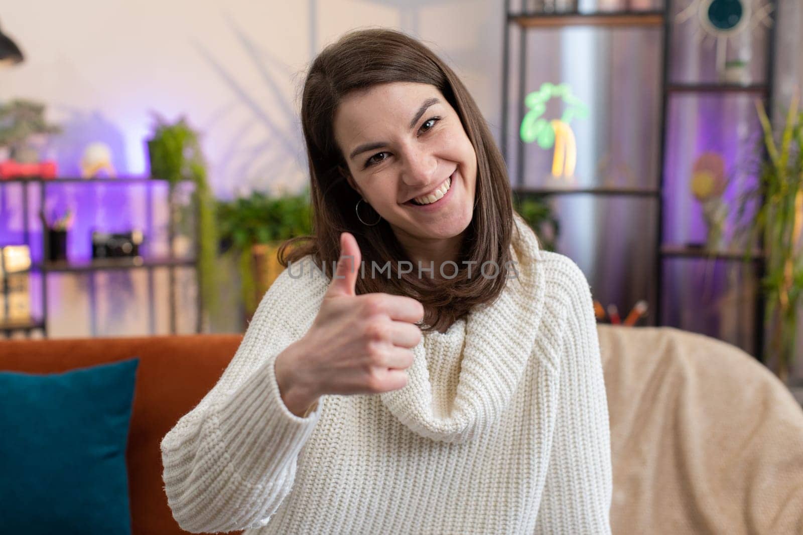 Like. Happy excited woman looking approvingly at camera showing thumbs up, like sign positive something, good great news, positive feedback. Portrait of young girl sitting on couch at home living room