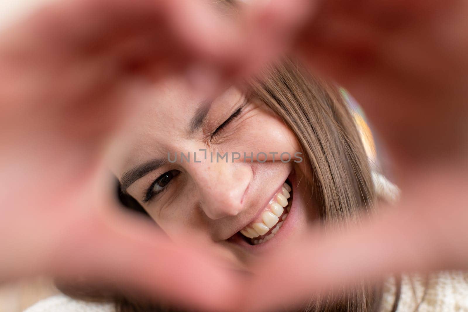 I love you. Happy young woman at home living room couch makes symbol of love, showing heart sign to camera, express romantic feelings express sincere positive feelings. Charity, gratitude, donation