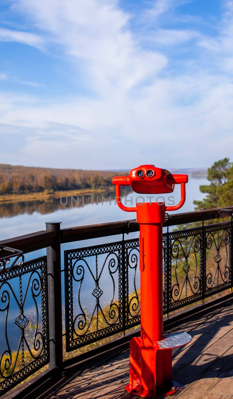 Public stationary binoculars on the banks of the river in summer or autumn to look at nature, coin-operated red metal binoculars.