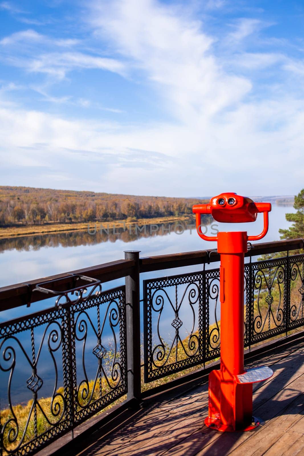 Public stationary binoculars on the banks of the river in summer or autumn to look at nature, coin-operated red metal binoculars.