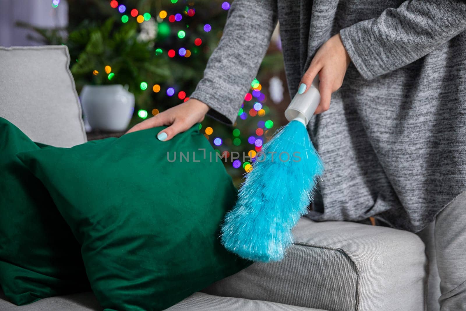 During a thorough cleaning, a woman picks up a pillow and sweeps up dust lying on the sofa. Taking care of order and tidiness throughout the house during all kinds of world.