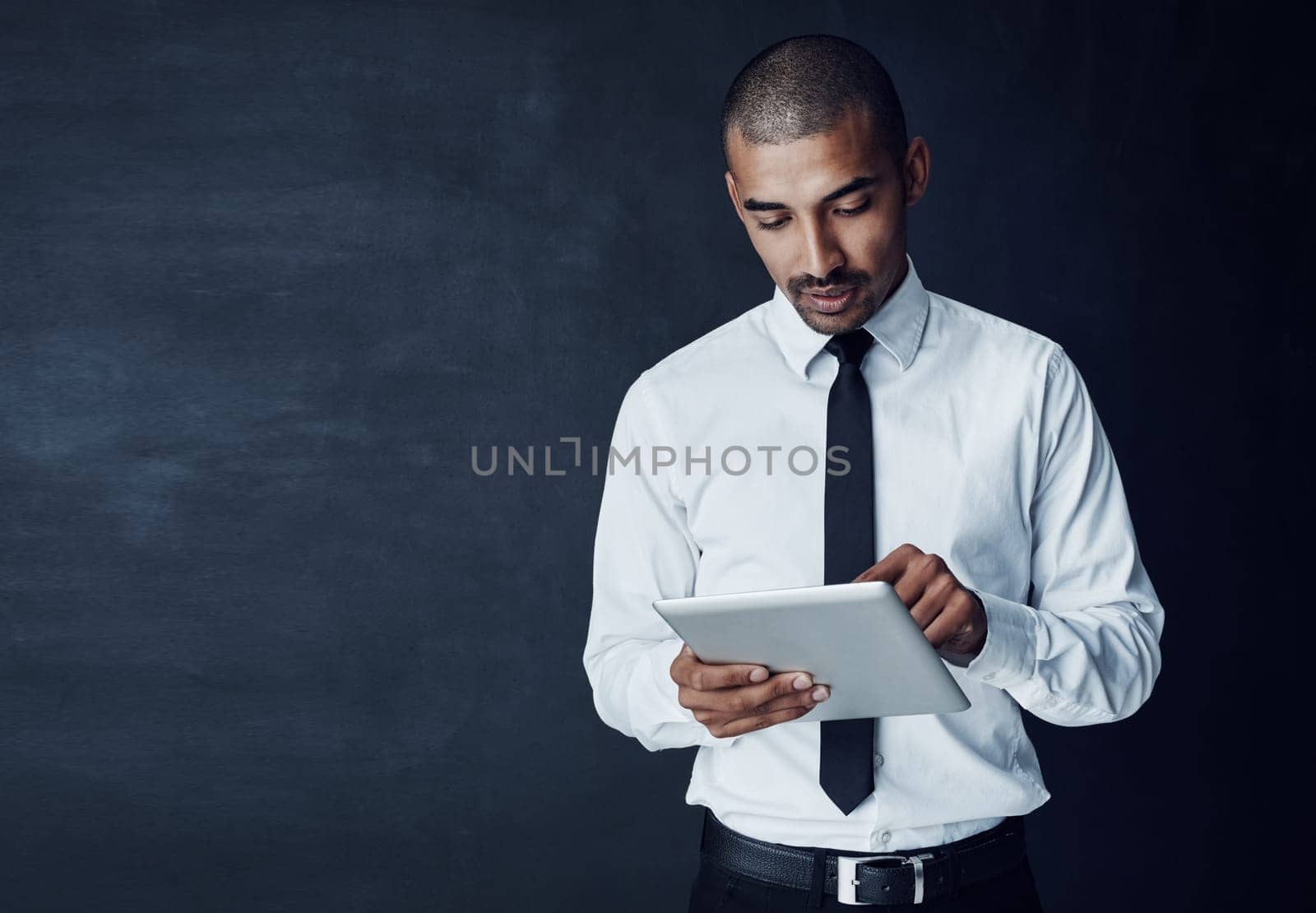 There to help you take care of the hard work. Studio shot of a young businessman using a digital tablet against a dark background. by YuriArcurs