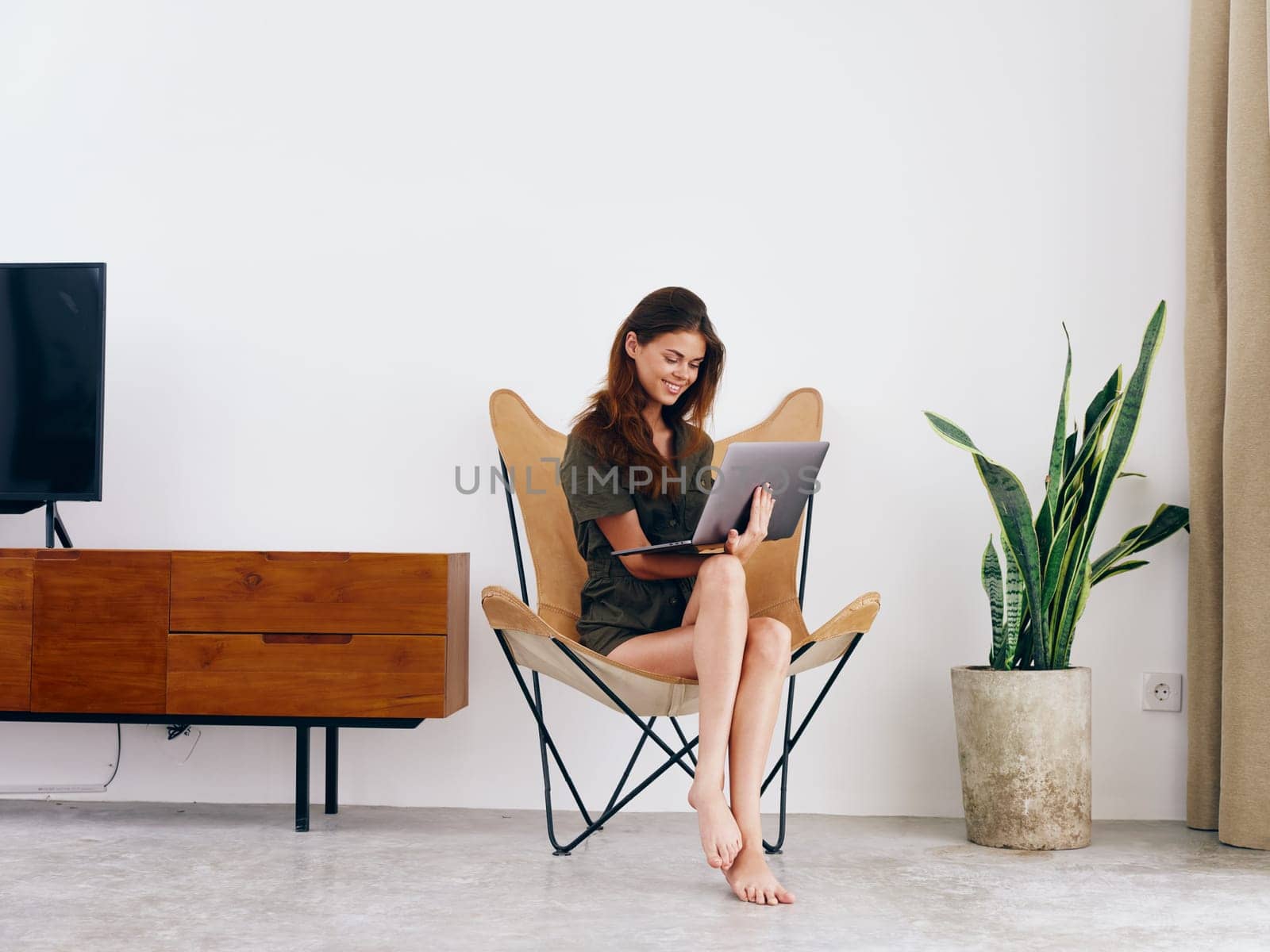 Female student study sits on a chair with a laptop work at home smile and relax, modern stylish interior Scandinavian lifestyle, copy space. by SHOTPRIME