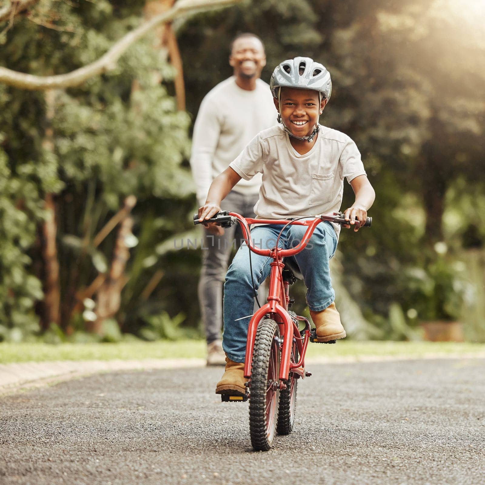 Boy with smile on bicycle, father and learn cycling with help, helmet for safety and family in park. Support, motivation and trust, black man and young kid outdoor, teaching and learning bike riding.